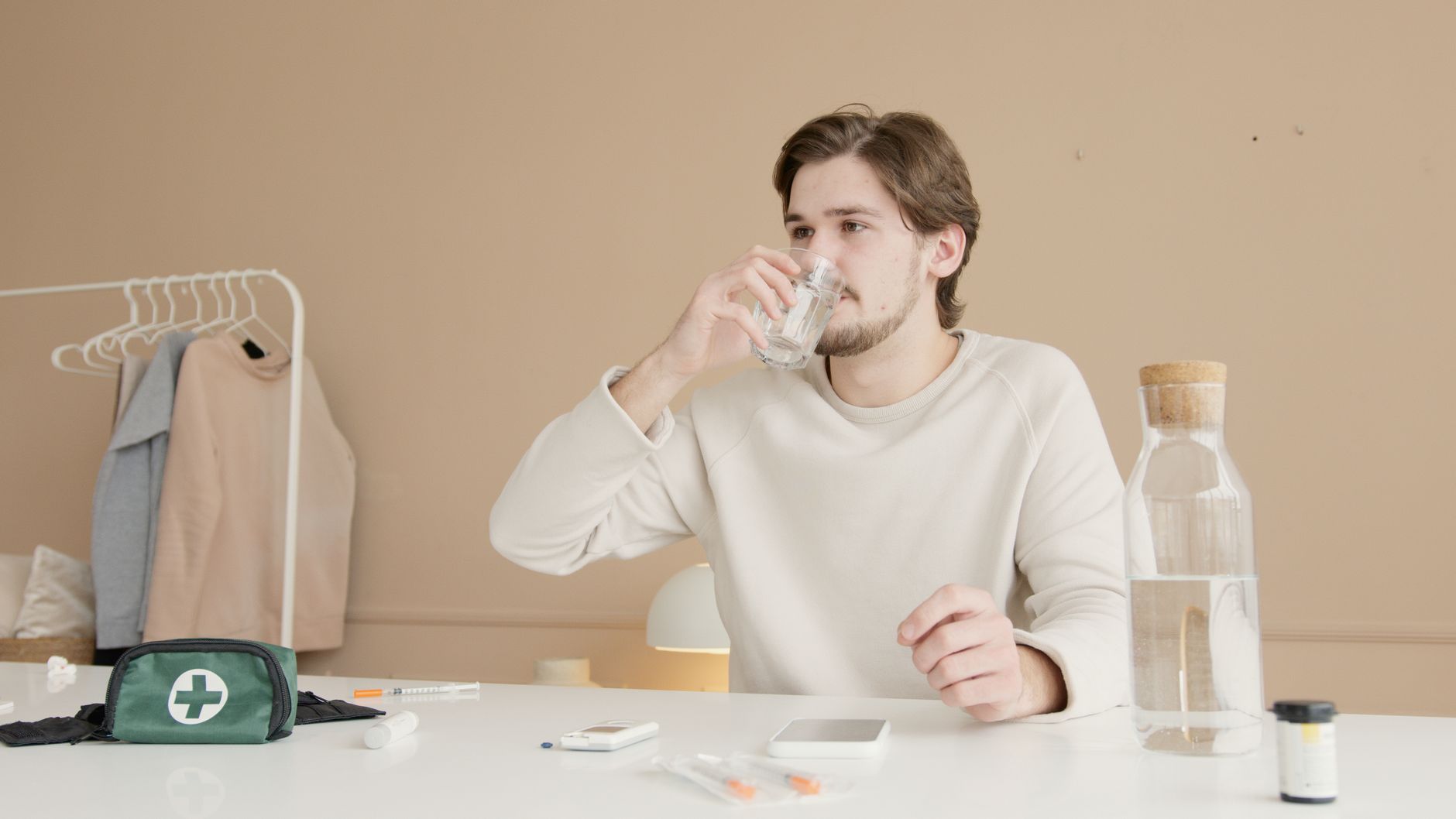 Natriumtekort simptome agter hoofpyn en verwardheid Natuurlike Medisyne Man in white long sleeves drinking water from glass at home with medical supplies.
