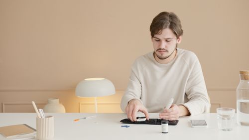 Free Young man checks blood glucose with a glucometer at home. Diabetes care and monitoring. Stock Photo