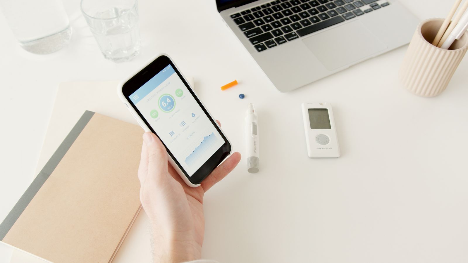 Person reviewing glucose readings on a smartphone beside diabetes monitoring equipment