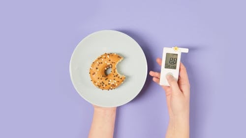 Free Person Holding a Glucometer and a Plate with a Donut  Stock Photo