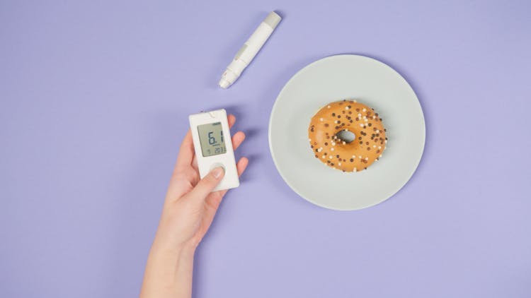 A Hand Holding A Glucometer Beside A Doughnut