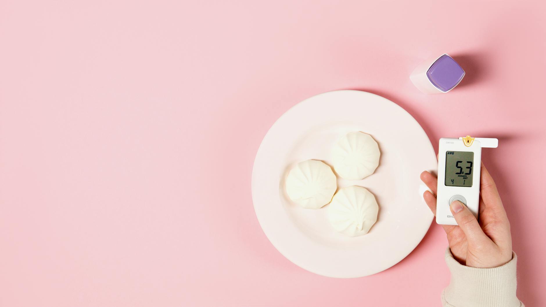 Flat lay of glucose meter and white sweets on a pink background, symbolizing diabetes awareness