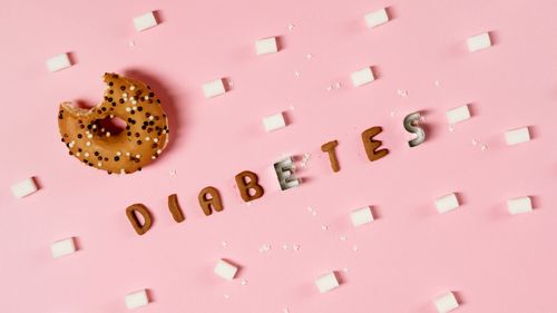 Free Creative depiction of diabetes with a donut, sugar cubes, and letters on a pink background. Stock Photo