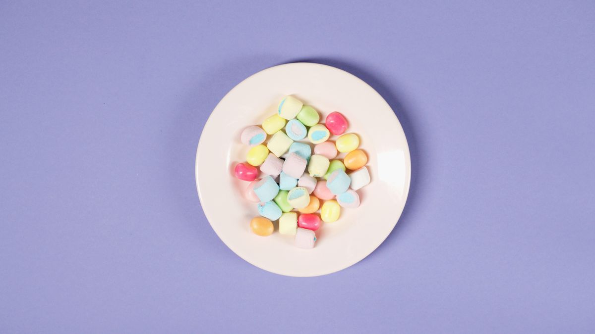 Top view of colorful marshmallows and candies on a white plate against a purple background.