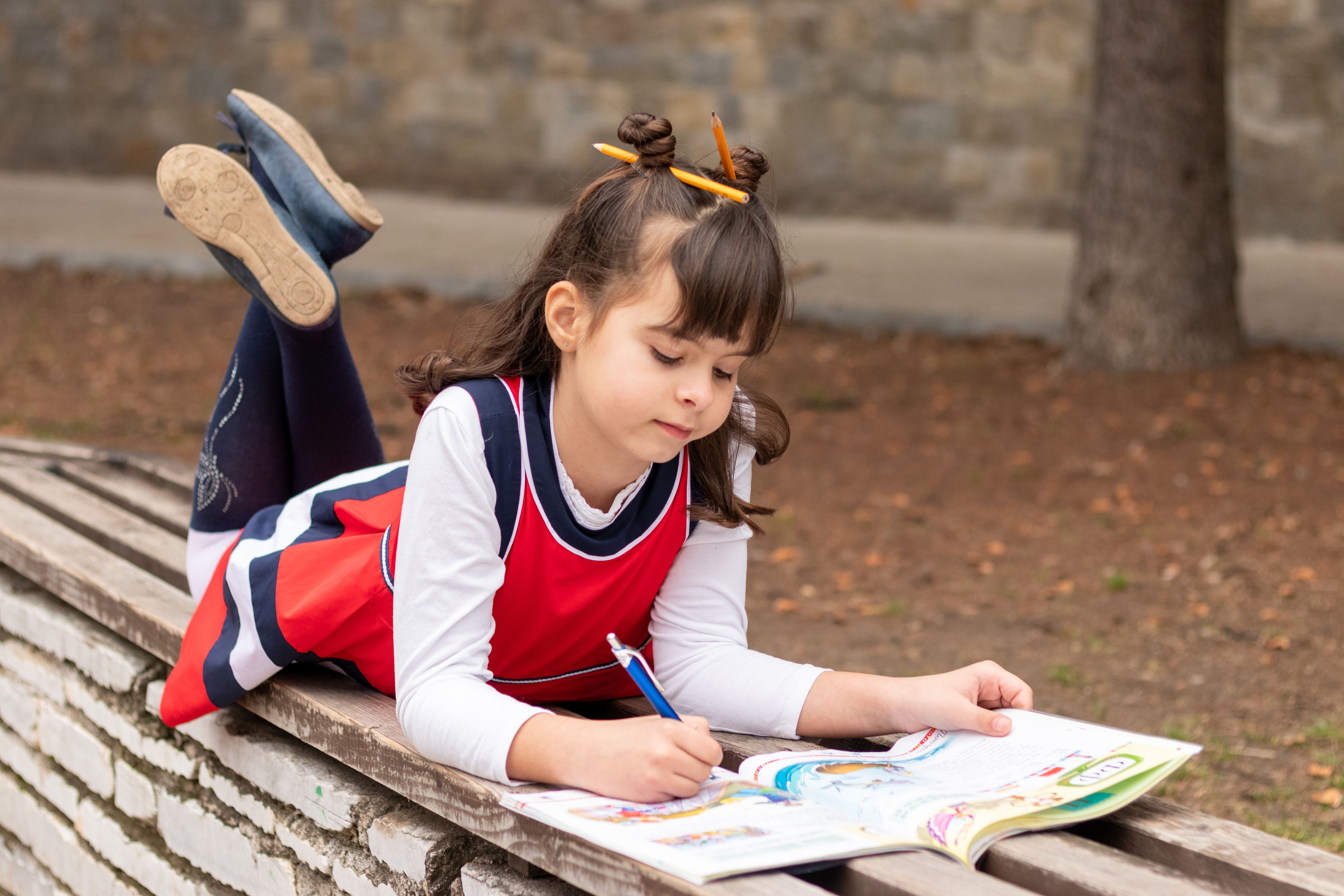 Portrait of a girl lying outdoors, engaged in coloring a book on a fall day.