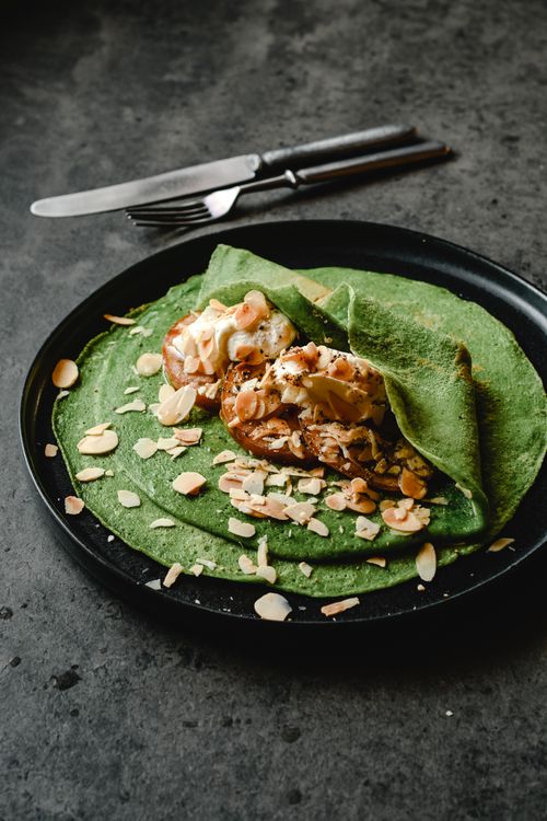Free Appetizing green pancake served on a black plate, garnished with almonds and cream, perfect for a healthy breakfast. Stock Photo