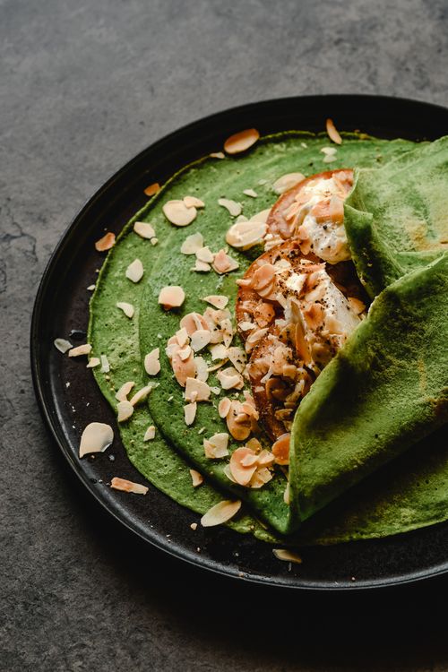 Free Delicious green spinach crepes served with cream cheese and almond flakes on a black plate. Stock Photo