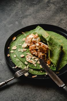 Close-up of spinach crepe with cream cheese and almonds on a dark plate, perfect for breakfast.