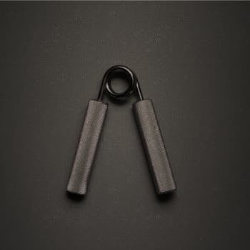 Close-up of a metallic hand grip exerciser placed on a dark textured surface for fitness and strength training.