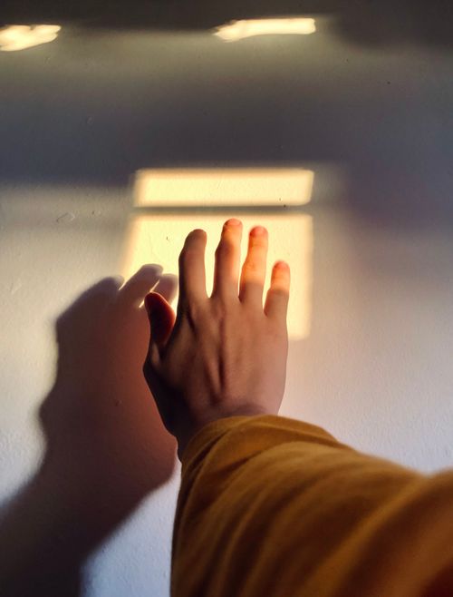 Free A hand reaches toward a sunlit wall, capturing a warm shadow and light play. Stock Photo