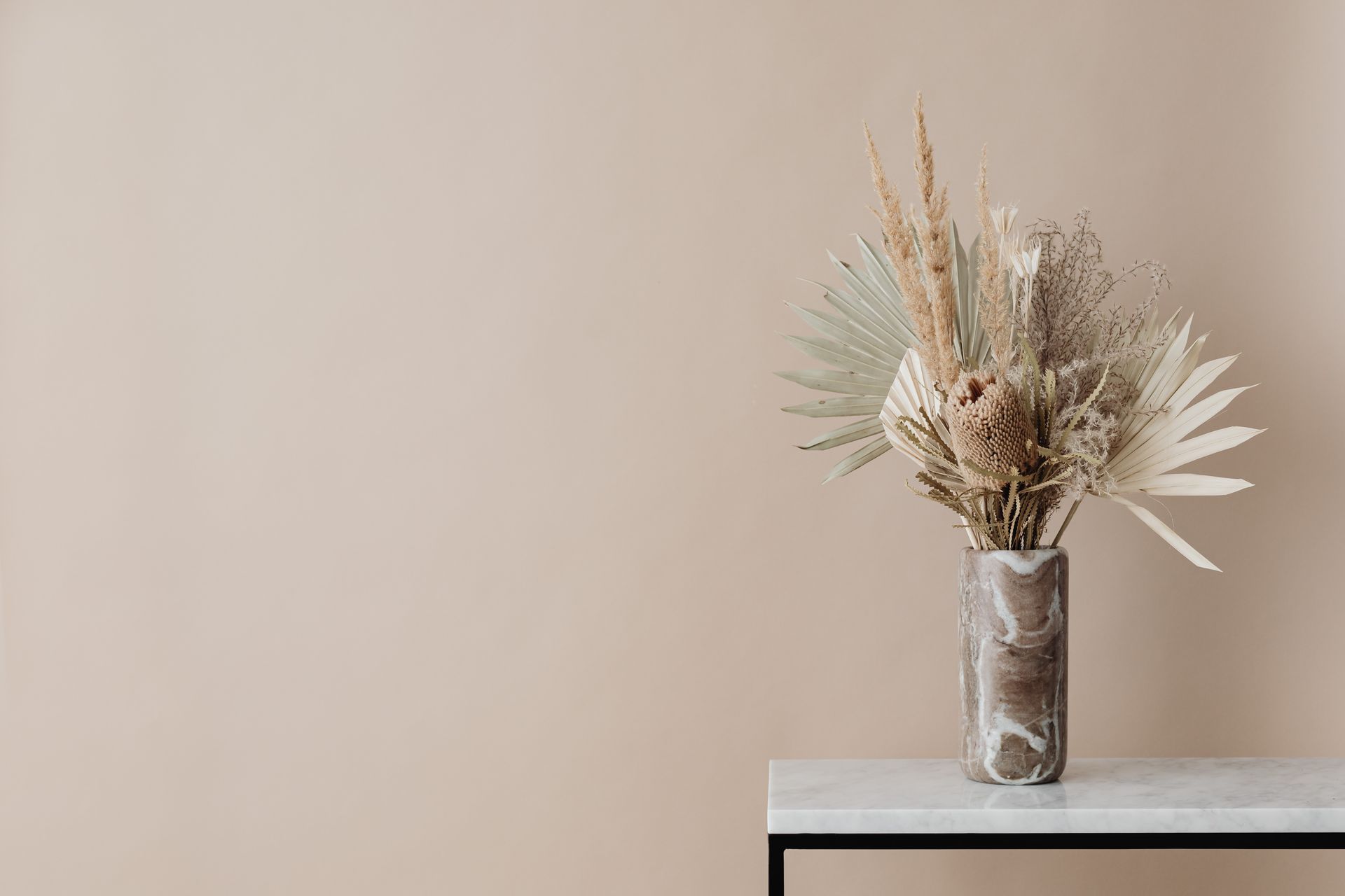 A minimalist dried floral arrangement in a marble vase on a table against a neutral background.