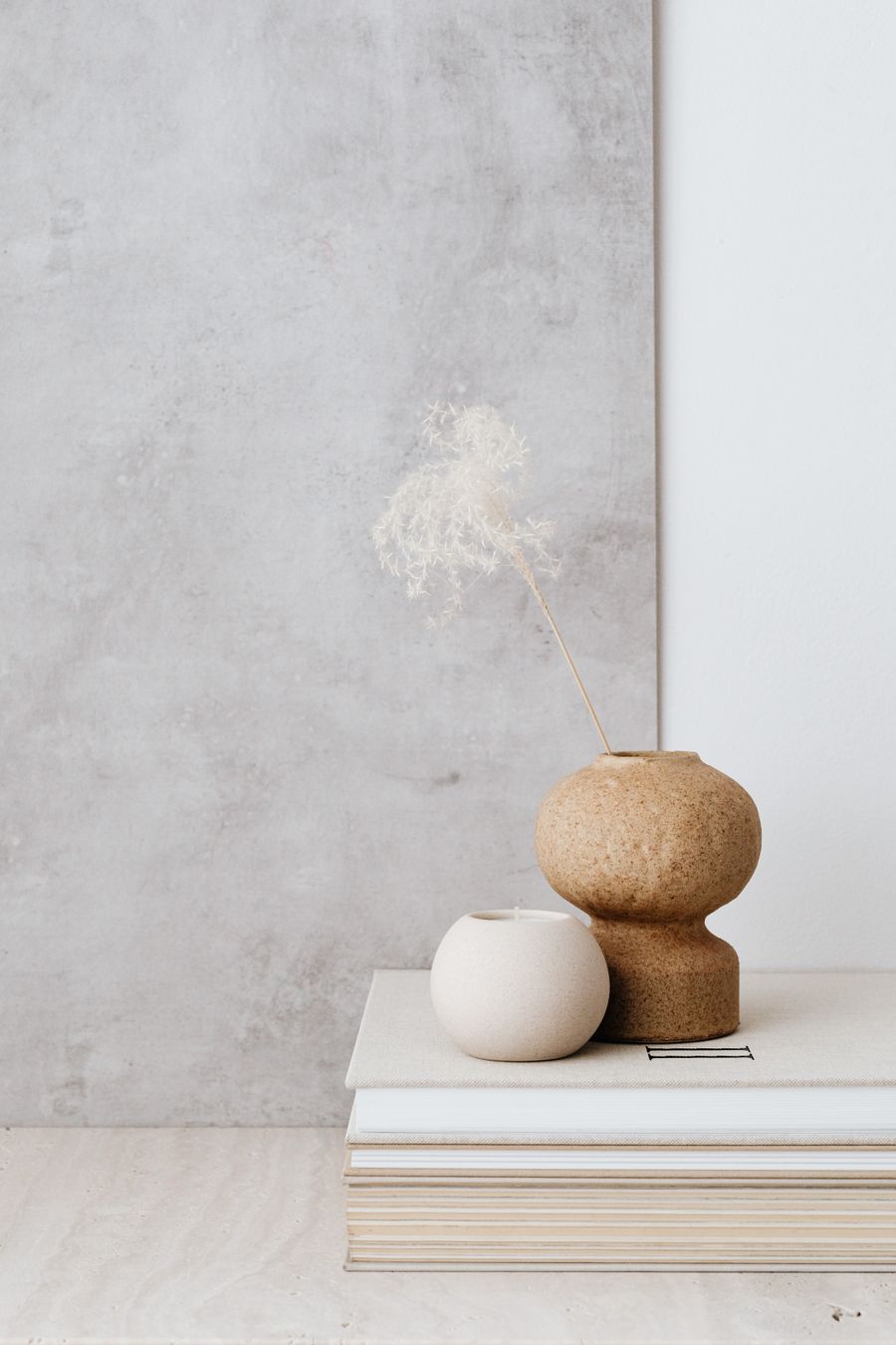 Minimal vases resting on a stack of books against a concrete wall
