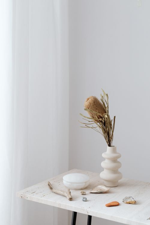 Free A serene still life of a table with a vase, stones, and driftwood against a white background. Stock Photo