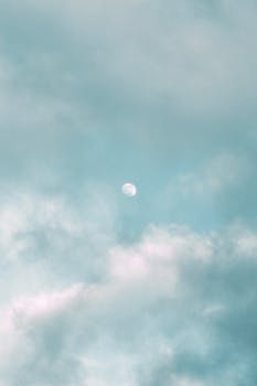 Tranquil clouds surrounding the moon on a clear day, embodying peace and calm.