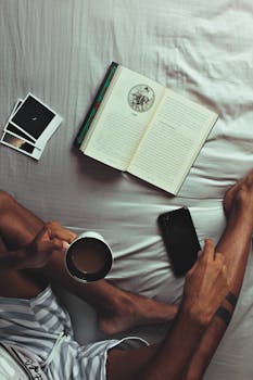 A cozy morning scene with a man reading in bed, enjoying coffee and photos.
