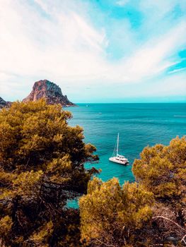 Breathtaking view of a yacht sailing near a rocky island, surrounded by lush trees.