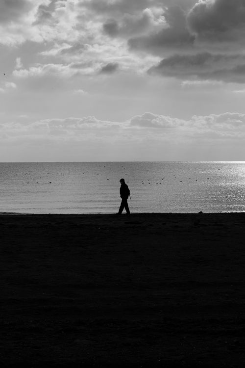 Free A lone figure walks along the serene beach under dramatic clouds. Stock Photo