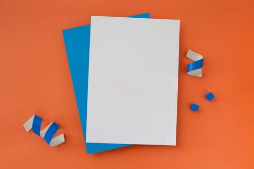 Free Flat lay of blank paper on orange background with blue accents for creative projects. Stock Photo