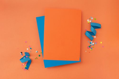 Free Bright orange and blue paper sheets with confetti and ribbon on orange background. Stock Photo