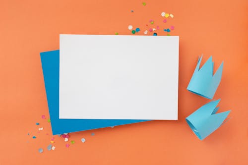 White and Blue Paper with Blue Paper Crowns and Confetti on Orange Background