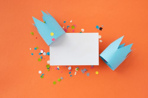 Free Colorful celebration scene with two paper crowns, confetti, and a blank card on vibrant orange. Stock Photo