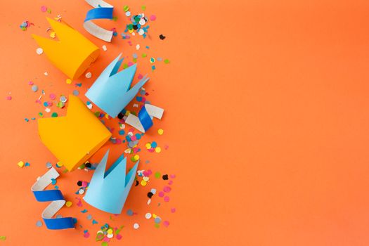 Bright paper crowns on orange surface surrounded by colorful confetti, perfect for party themes.
