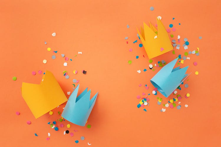 Paper Crowns And Confetti Over Orange Surface