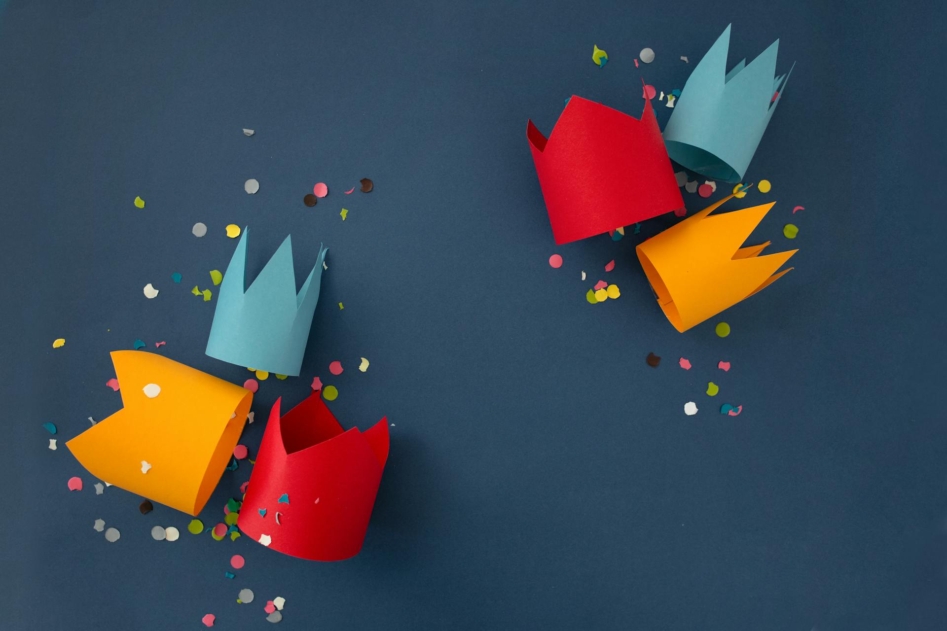 Bright and festive paper crowns with confetti on a blue background, perfect for celebrations.