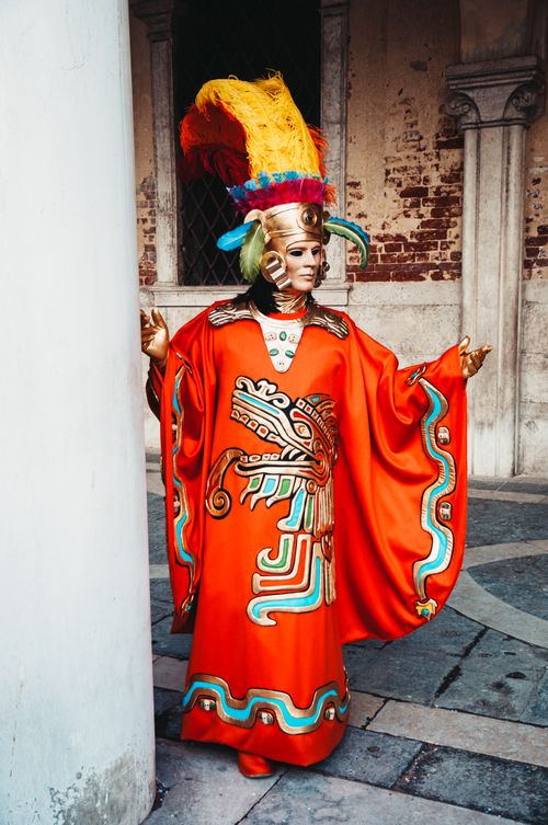 Free Intricate Venetian carnival costume with feathered mask in vibrant colors outside historical building. Stock Photo