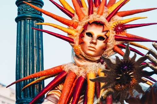 Free Vibrant Venetian mask with intricate sun rays at a festival. Perfect for cultural and artistic themes. Stock Photo