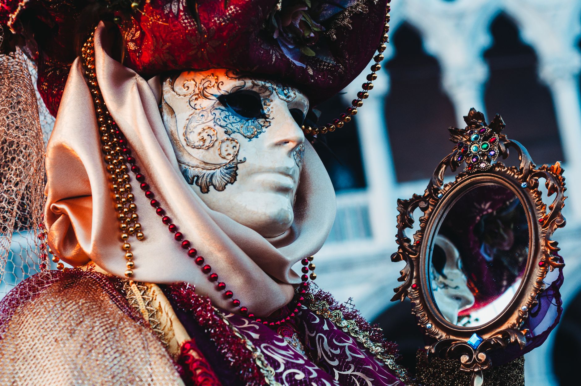 Masked figure in ornate costume holds decorative mirror at Venice's famous masquerade.