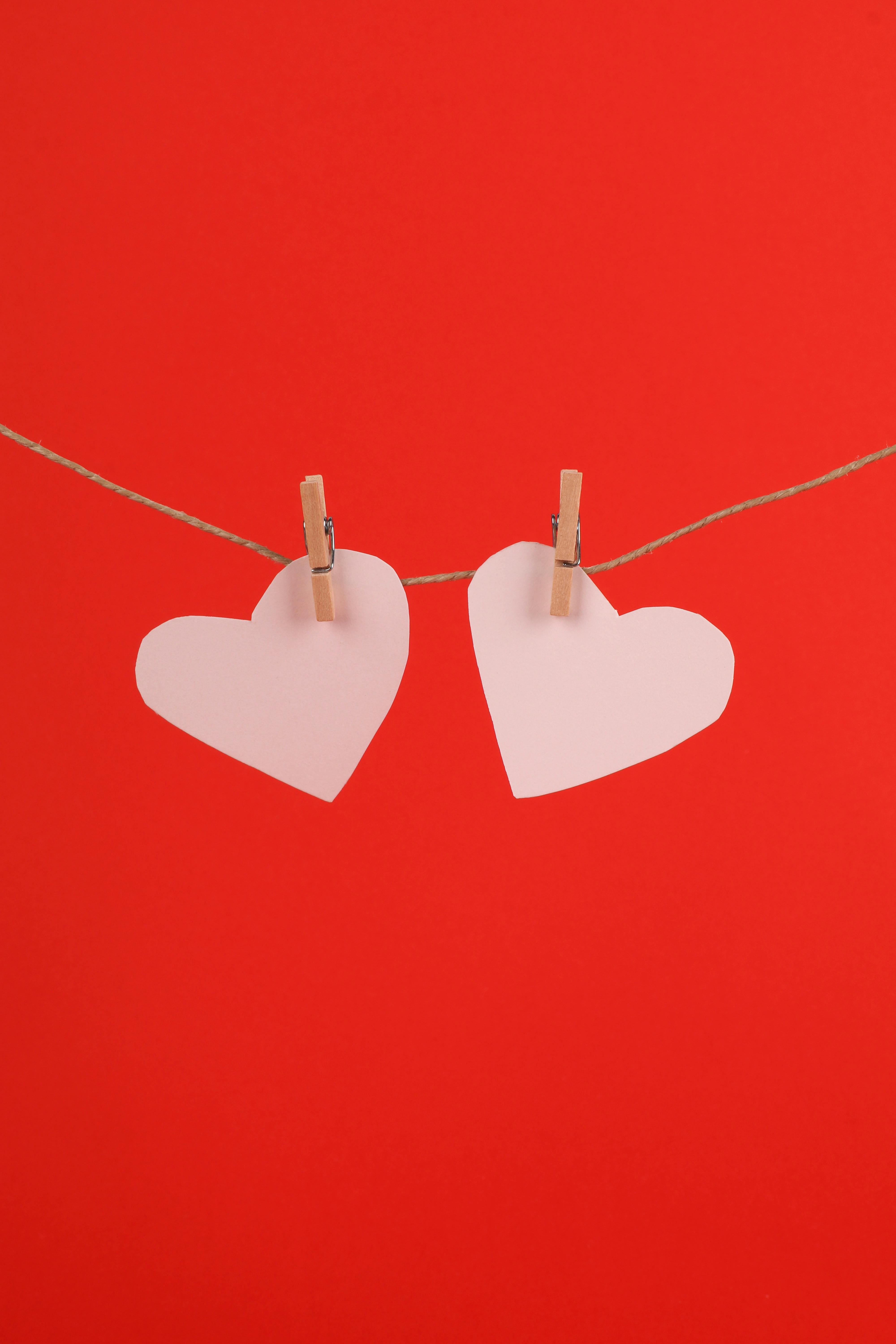 Two paper hearts clipped to a line against a vibrant red backdrop, symbolizing love and romance.