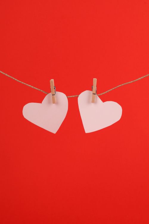 Free Two paper hearts clipped to a line against a vibrant red backdrop, symbolizing love and romance. Stock Photo