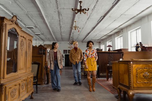 Three young adults exploring an antique store filled with vintage furniture pieces.