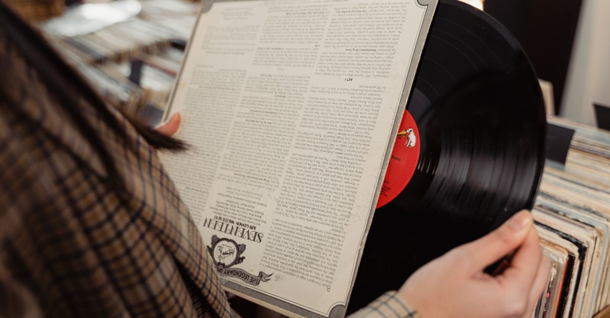 Close-up of hands holding a colorful, gatefold vinyl record, highlighting the large artwork and lyric sheet