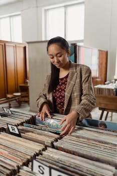 Woman looking through vinyl records in a retro-style music store, wearing a plaid jacket.