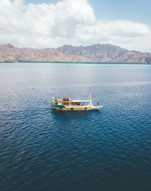 Free From above of boat floating on rippling peaceful water of sea with rocky coast under cloudy blue sky Stock Photo