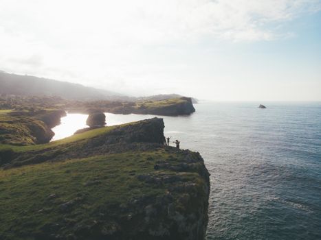 Cliff Covered with Grass Beside Sea Under White Sky