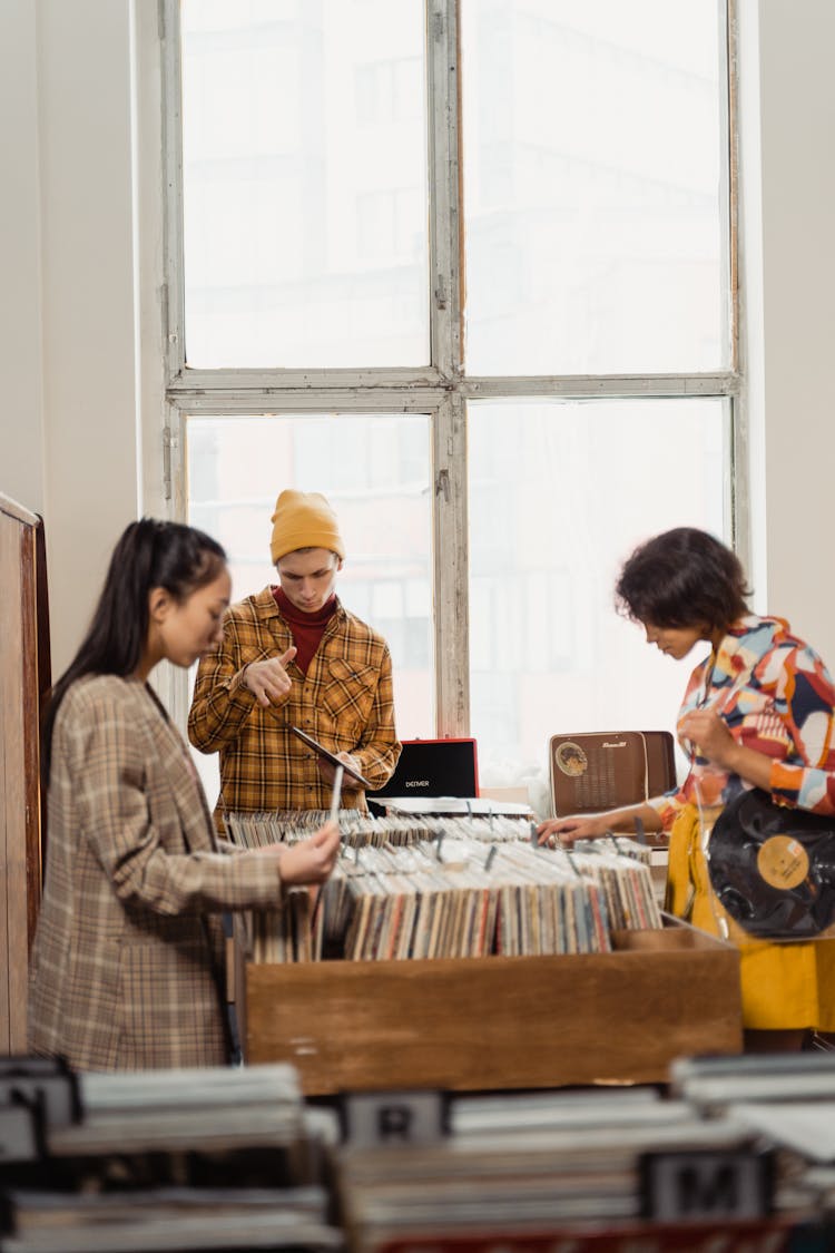 Two Women And Man Choosing Vinyl Record In Vintage Store