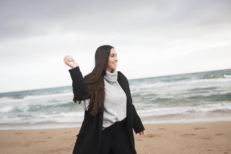 Woman In White Sweater And Black Jacket Holding White Ball On The Beach