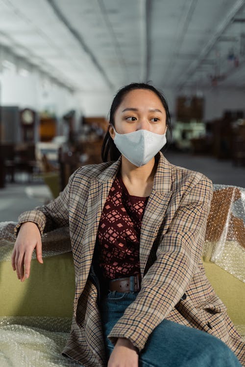 Woman Wearing A Plaid Blazer and Face Mask Sitting On A Couch