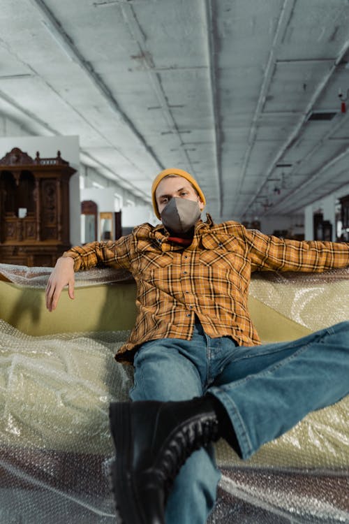 Man In Plaid Shirt With Face Mask Sitting On A Couch
