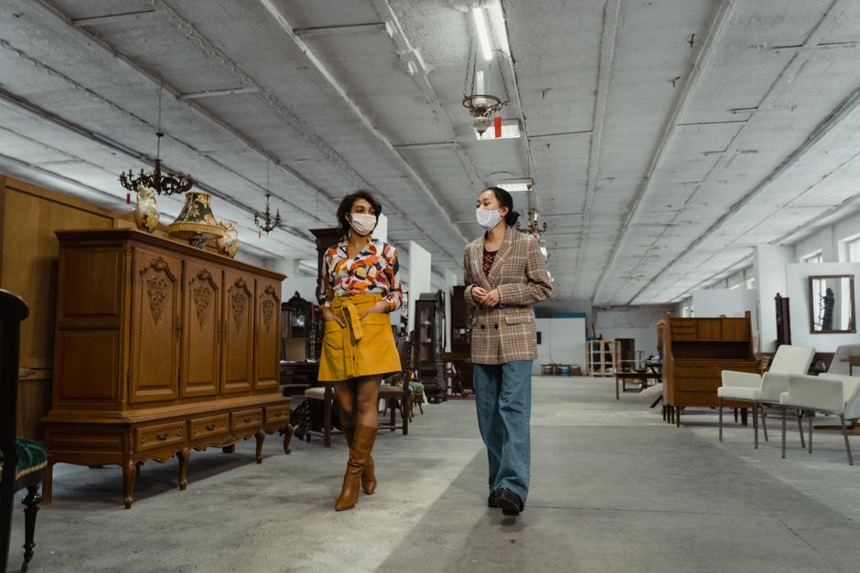 Two women wearing masks explore a vintage furniture store, highlighting fashion and the new normal.