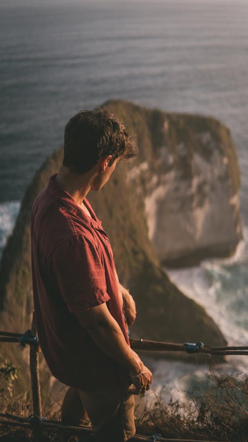 A Man in Red Shirt Looking Down at the Seashore