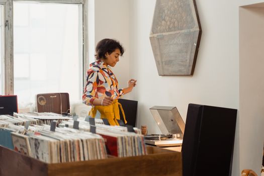 A woman enjoys browsing vinyl records and listening to music indoors in a stylish store.