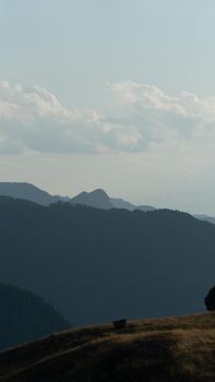 Tranquil mountain view with layered hills and soft cloud formations in daylight.