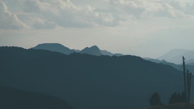 A peaceful landscape of silhouetted mountains against a cloudy sky at twilight.