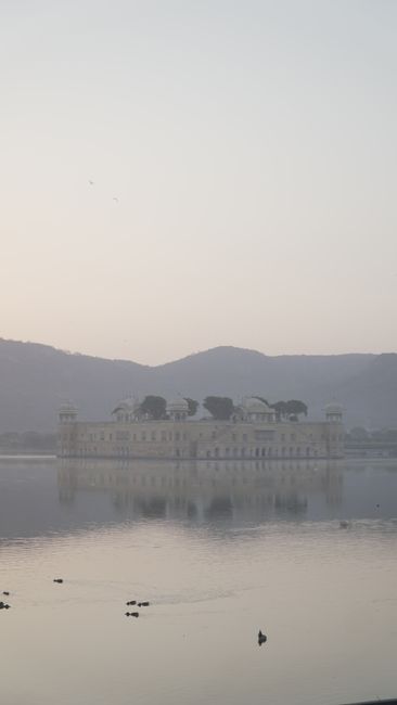 Serene view of Jal Mahal in Jaipur surrounded by misty waters and hills, creating a tranquil atmosphere.