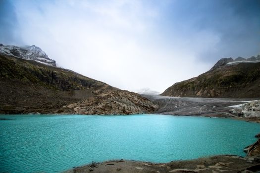 Breathtaking view of a turquoise alpine lake surrounded by snowy mountains in Obergoms, Switzerland.