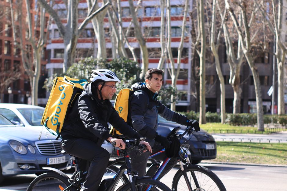 Dos hombres en bicicleta entregando comida en la ciudad de Madrid, mostrando servicios de entrega urbana.
